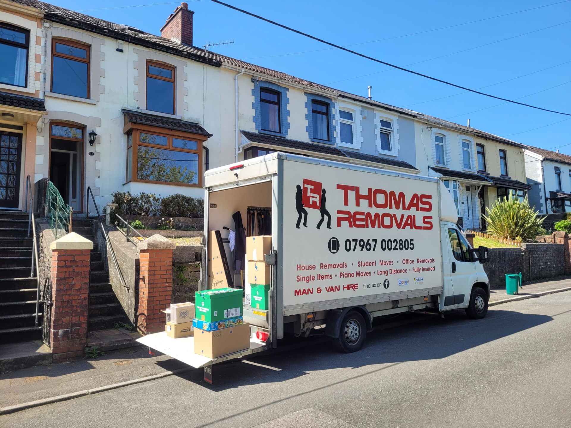 Thomas Removals van loaded with boxes and belongings outside a terraced house in Porth, South Wales