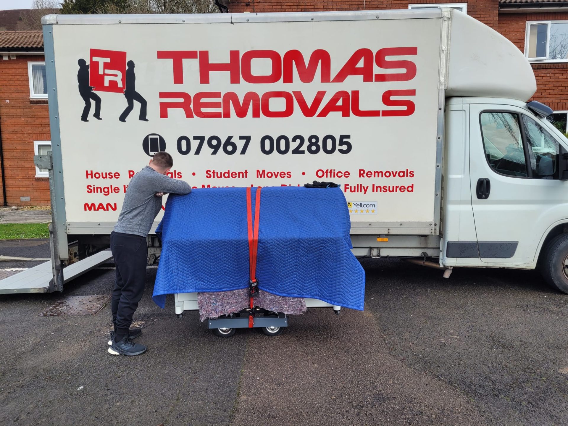 Thomas Removals team member securing a wrapped piano onto a specialist trolley for safe transport